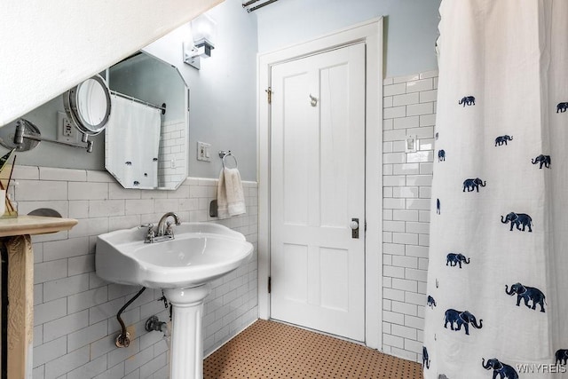 bathroom featuring a wainscoted wall, tile walls, and a sink