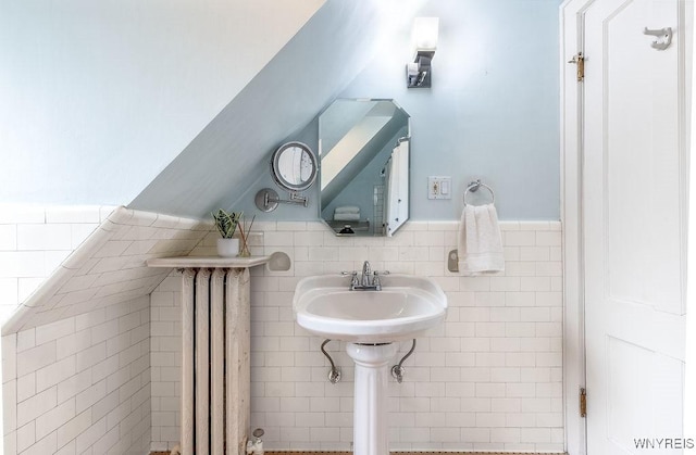 bathroom featuring a sink, tile walls, wainscoting, and vaulted ceiling