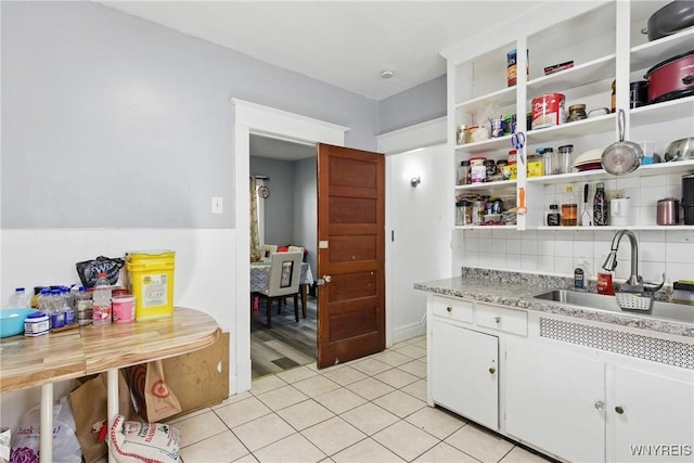 kitchen with a sink, open shelves, white cabinets, light countertops, and light tile patterned floors