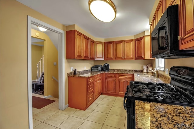 kitchen featuring light tile patterned floors, dark stone countertops, brown cabinetry, black appliances, and a sink