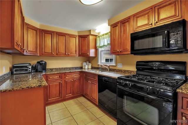 kitchen featuring light tile patterned floors, dark stone countertops, brown cabinets, black appliances, and a sink