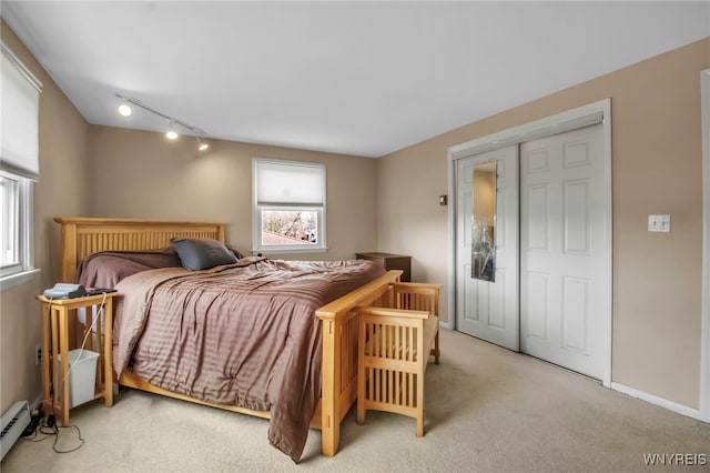 bedroom featuring a baseboard heating unit, light carpet, and baseboards