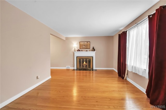 unfurnished living room featuring light wood finished floors, a fireplace with flush hearth, and baseboards