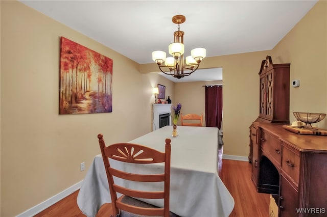 dining room with wood finished floors, a fireplace, baseboards, and a chandelier