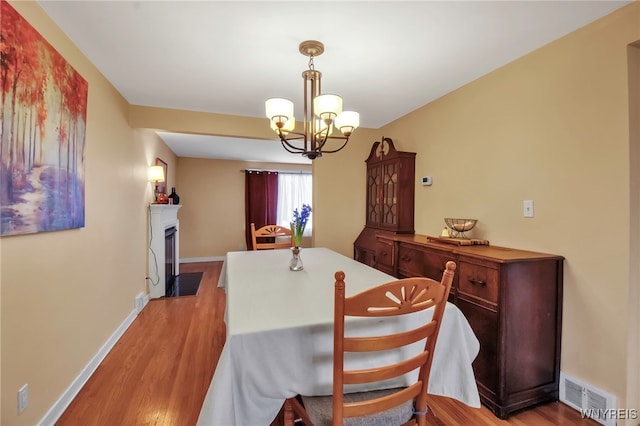 dining room featuring visible vents, an inviting chandelier, light wood-type flooring, and a fireplace with flush hearth