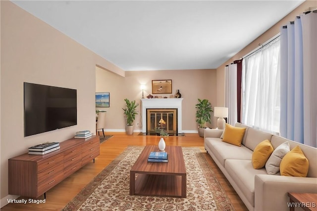 living room featuring a fireplace with flush hearth, baseboards, and light wood finished floors