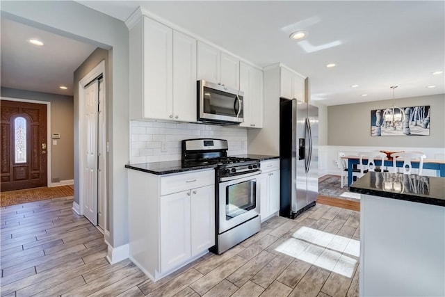 kitchen featuring backsplash, wood finish floors, stainless steel appliances, hanging light fixtures, and white cabinetry