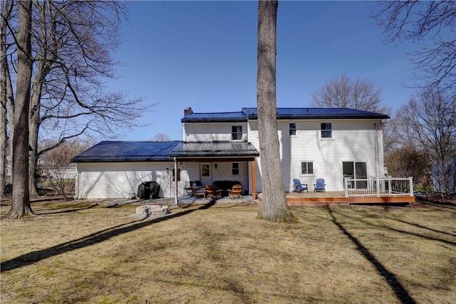 back of property featuring a lawn, a patio, a wooden deck, metal roof, and a chimney