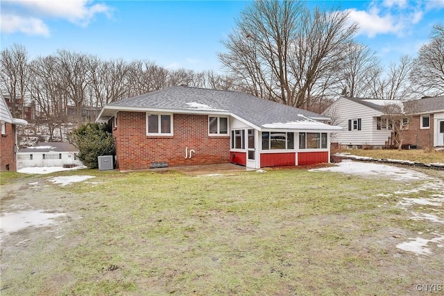 back of house featuring a lawn, roof with shingles, a sunroom, brick siding, and central AC unit