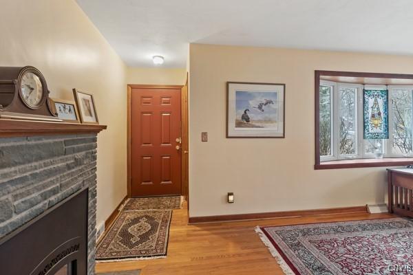 entrance foyer featuring a stone fireplace, light wood-style floors, and baseboards