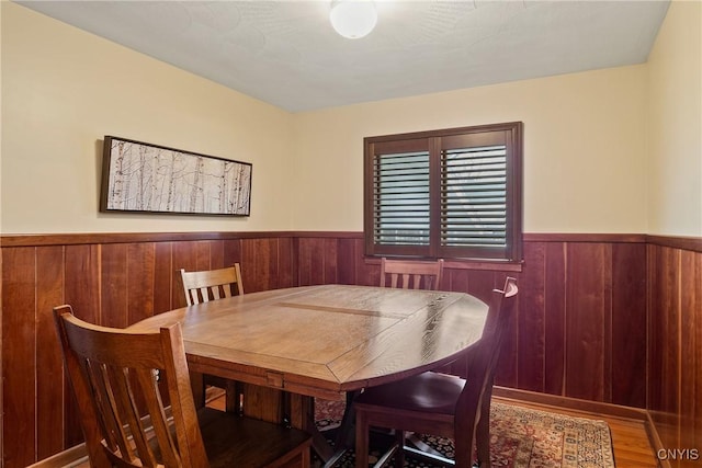 dining room with wood finished floors, wood walls, and wainscoting