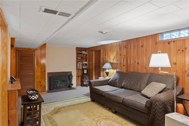 living room featuring a brick fireplace, wooden walls, carpet, and visible vents