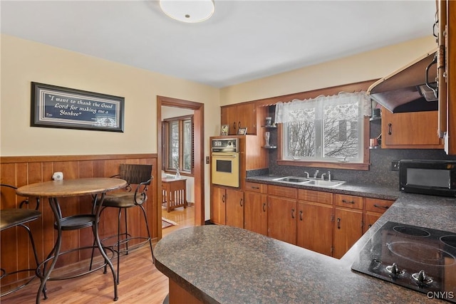 kitchen with oven, black electric stovetop, dark countertops, and a sink