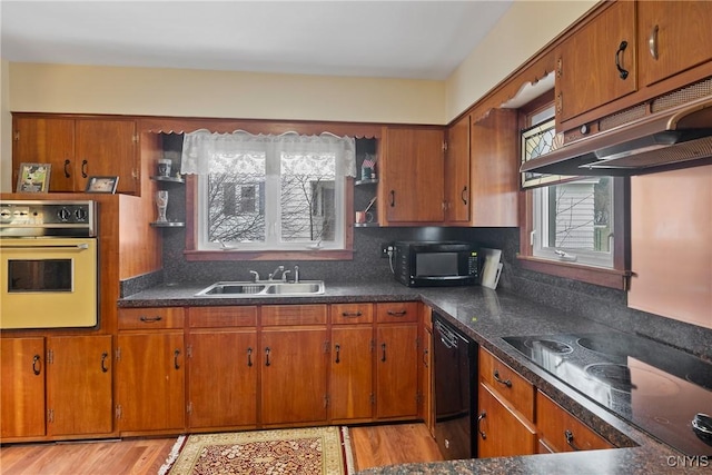 kitchen featuring black appliances, brown cabinets, under cabinet range hood, and a sink