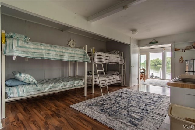 bedroom with access to exterior, beam ceiling, freestanding refrigerator, wood finished floors, and a sink