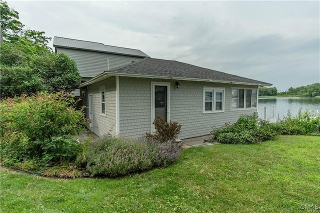 rear view of property with a yard, a water view, and roof with shingles