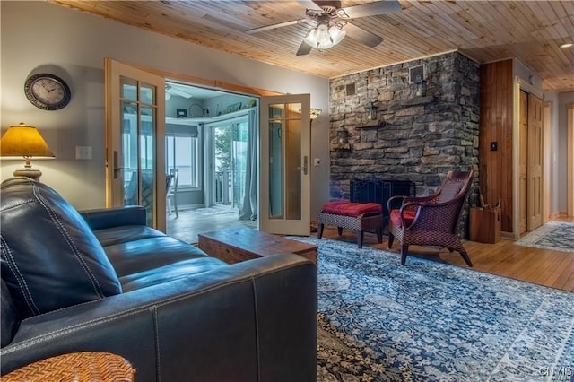 living room featuring ceiling fan, wood ceiling, vaulted ceiling, a stone fireplace, and wood finished floors