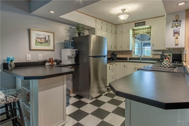 kitchen featuring a breakfast bar, dark countertops, freestanding refrigerator, a peninsula, and light floors