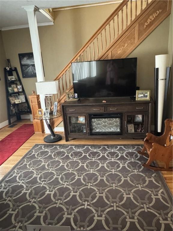 living area featuring decorative columns, baseboards, light wood-type flooring, and ornamental molding