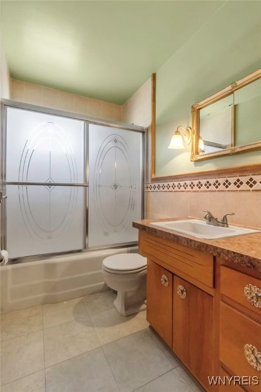 bathroom featuring tile patterned floors, toilet, vanity, enclosed tub / shower combo, and tile walls