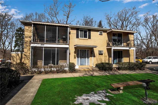 back of property featuring a balcony, a yard, brick siding, and a sunroom