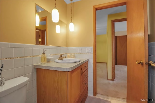 bathroom with a wainscoted wall, toilet, tile walls, and vanity