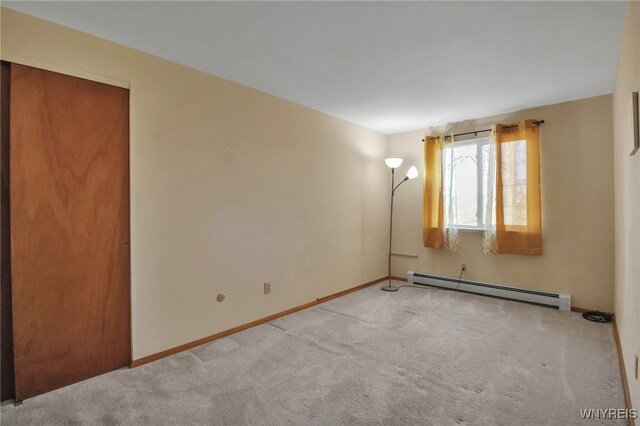 spare room featuring a baseboard heating unit, baseboards, and light colored carpet