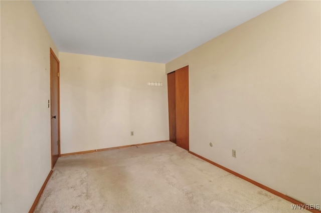 spare room featuring light colored carpet and baseboards