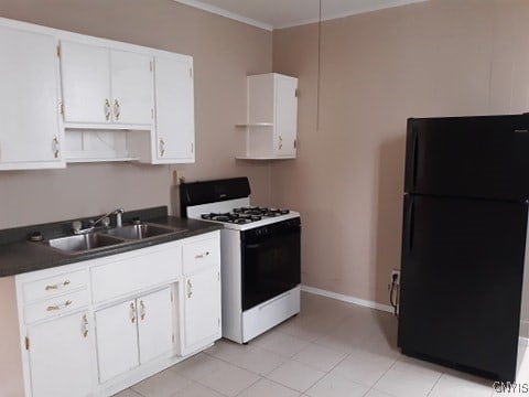 kitchen featuring dark countertops, white gas range oven, freestanding refrigerator, white cabinetry, and a sink