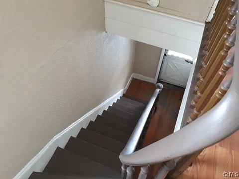 stairway with baseboards, wood finished floors, and a textured wall