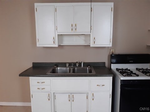 kitchen with a sink, range with gas cooktop, dark countertops, and white cabinetry