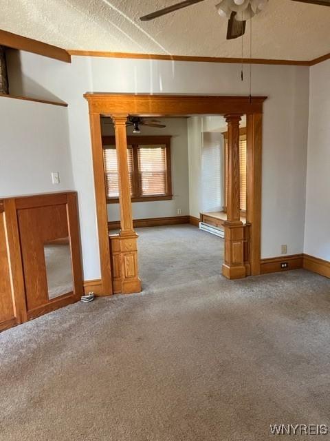 carpeted empty room featuring baseboards, decorative columns, ceiling fan, a textured ceiling, and crown molding