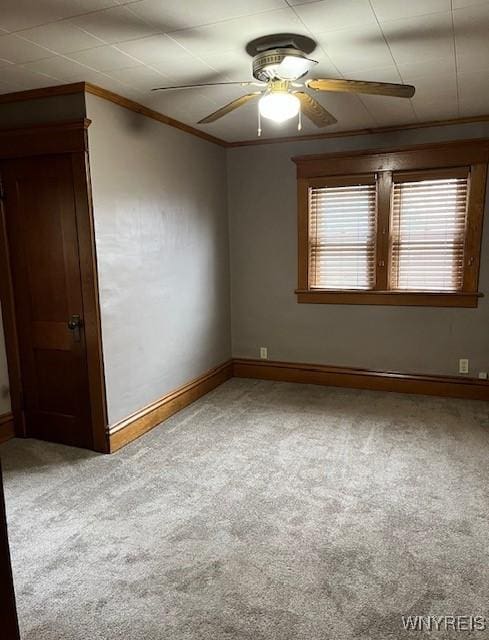 carpeted spare room featuring ceiling fan, baseboards, and ornamental molding