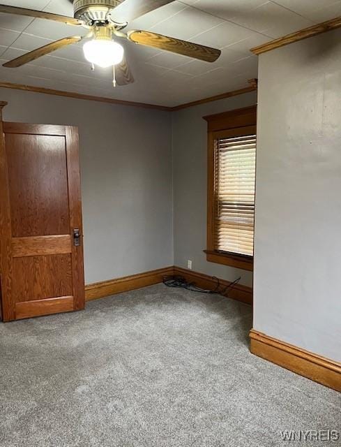 empty room with carpet flooring, ceiling fan, crown molding, and baseboards