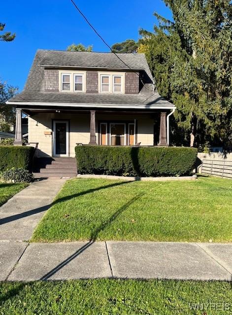 view of front facade with a front lawn, fence, and a shingled roof