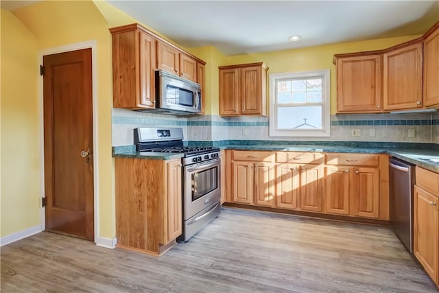 kitchen featuring decorative backsplash, dark countertops, light wood-type flooring, and appliances with stainless steel finishes