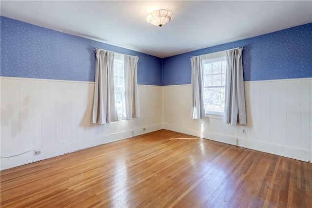 unfurnished room featuring wallpapered walls, wood finished floors, and wainscoting