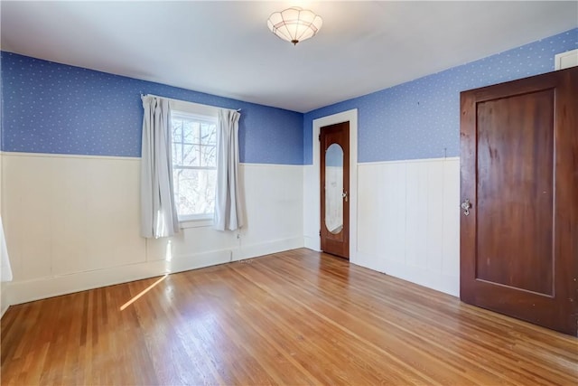 spare room featuring wood finished floors, wainscoting, and wallpapered walls