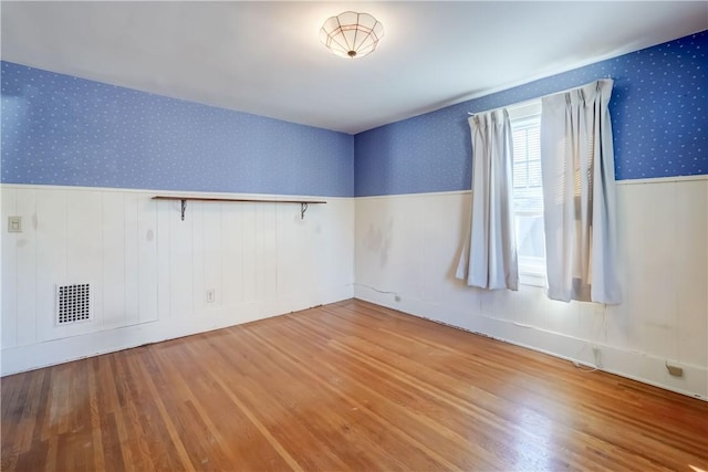 spare room featuring a wainscoted wall, visible vents, wood finished floors, and wallpapered walls