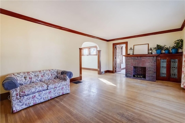 living room featuring wood finished floors, baseboards, arched walkways, ornamental molding, and a brick fireplace