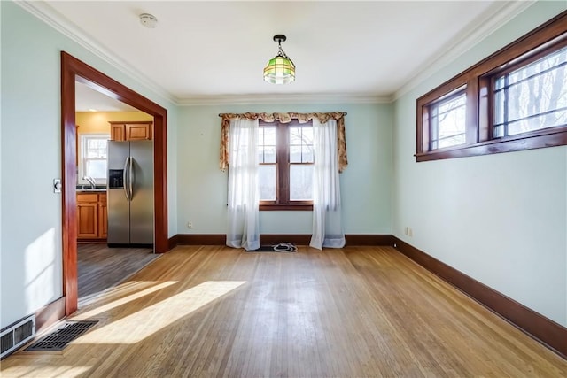 unfurnished dining area with light wood-type flooring, baseboards, visible vents, and crown molding