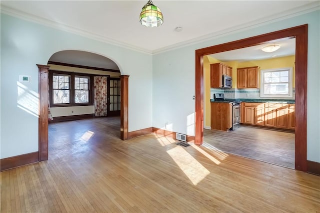 interior space featuring baseboards, light wood-style floors, arched walkways, and ornamental molding