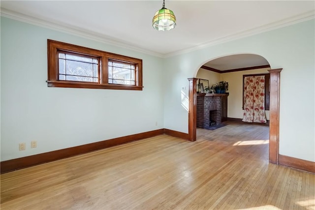 spare room featuring light wood-style flooring, ornamental molding, arched walkways, a fireplace, and baseboards