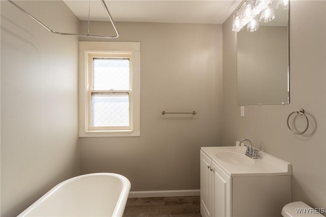 full bath with toilet, wood finished floors, baseboards, a soaking tub, and vanity