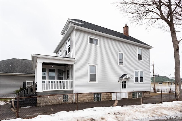 view of snowy exterior featuring a fenced front yard, covered porch, and a chimney