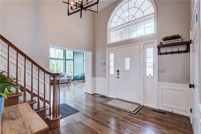 foyer entrance with dark wood-type flooring, stairway, plenty of natural light, and a wainscoted wall