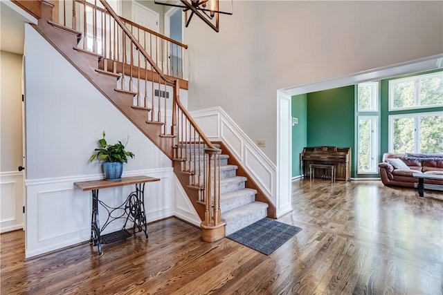 staircase featuring an inviting chandelier, wood finished floors, a towering ceiling, and a decorative wall