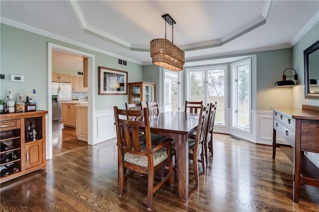 dining room with a tray ceiling, dark wood-type flooring, a wainscoted wall, and ornamental molding