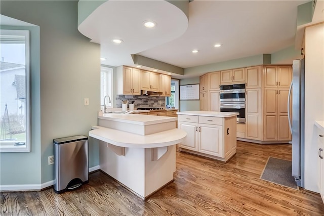 kitchen featuring a peninsula, a sink, light countertops, appliances with stainless steel finishes, and light wood-type flooring