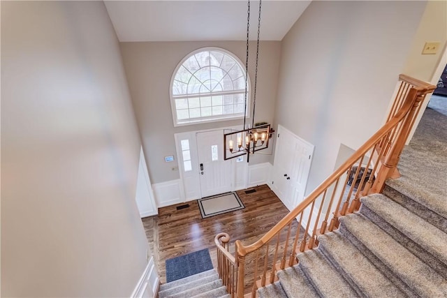 foyer featuring stairway, wood finished floors, a towering ceiling, wainscoting, and a notable chandelier